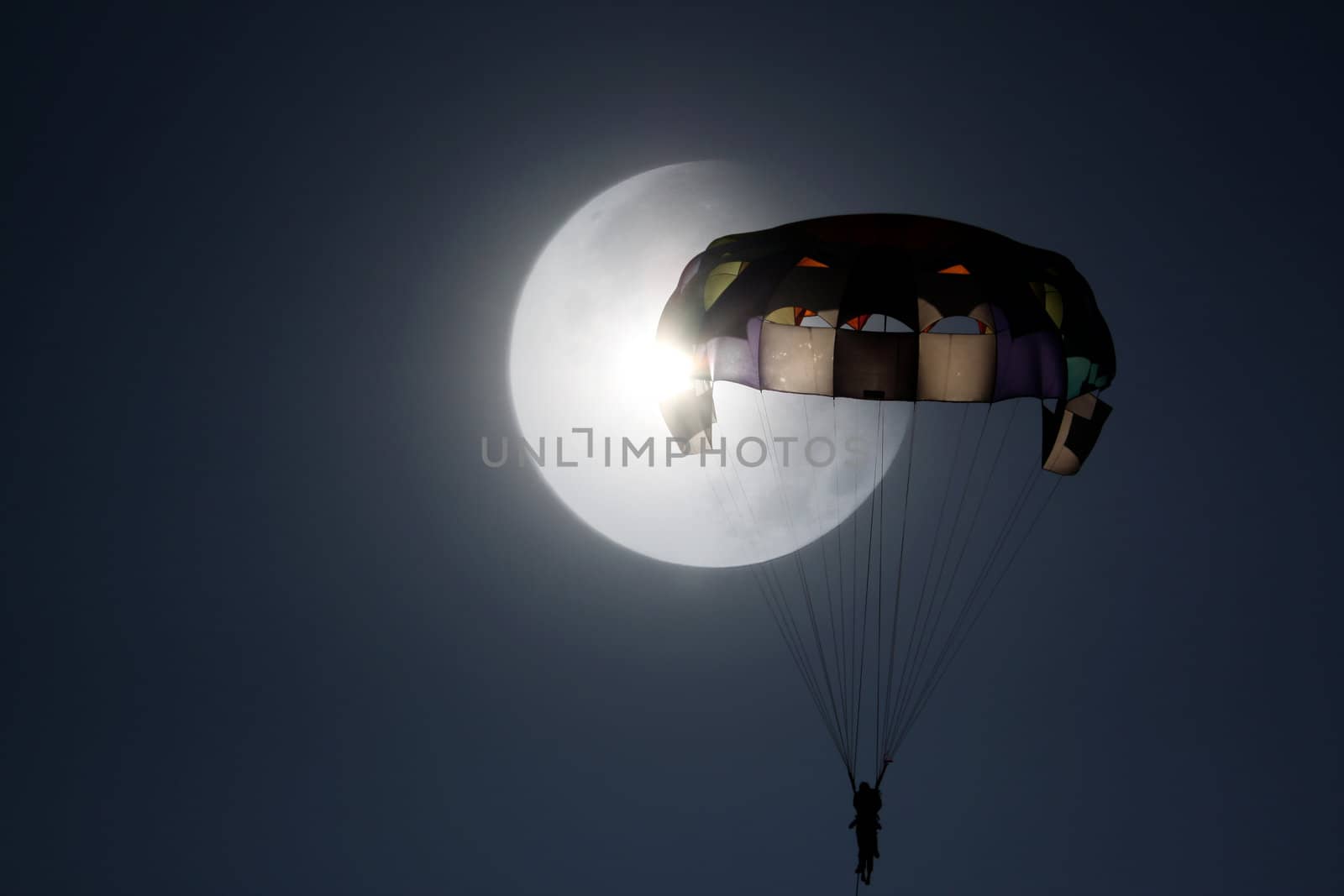 A beautiful view of a parasailing person on the backdrop of a huge moon.