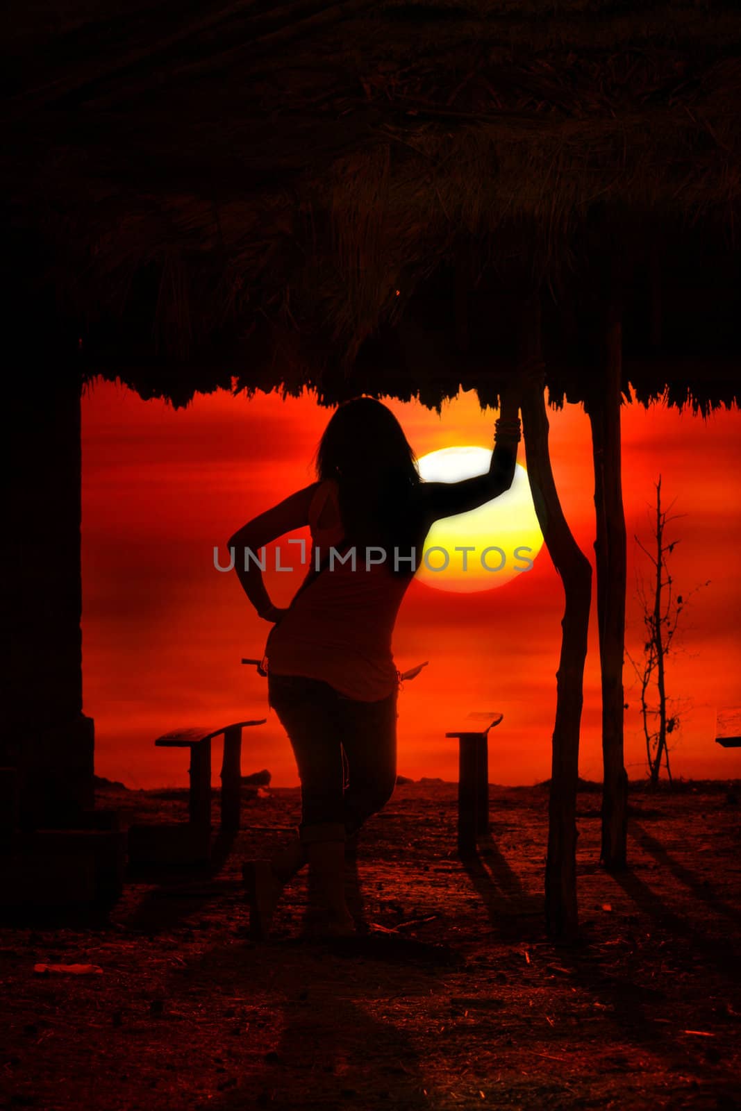 A woman watching a dark tropical sunset with a huge sun.