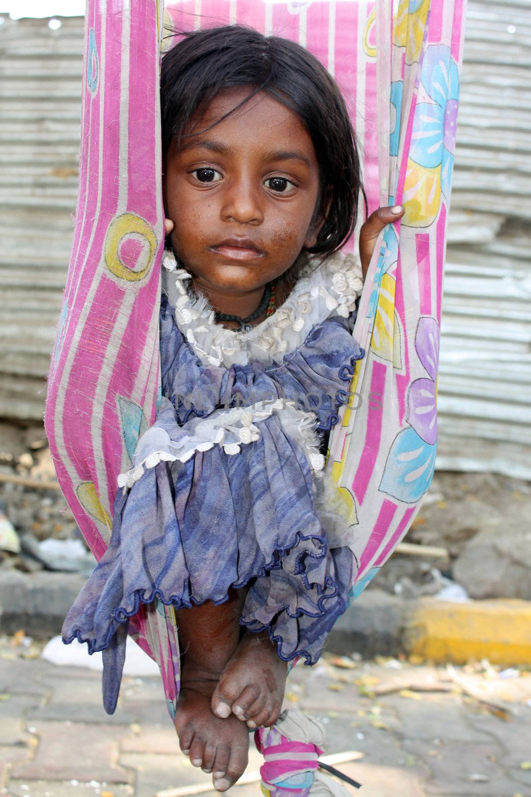 The very poor sick Indian girl sitting in a swing made of an old sari (traditional women clothes), lost in her thoughts.