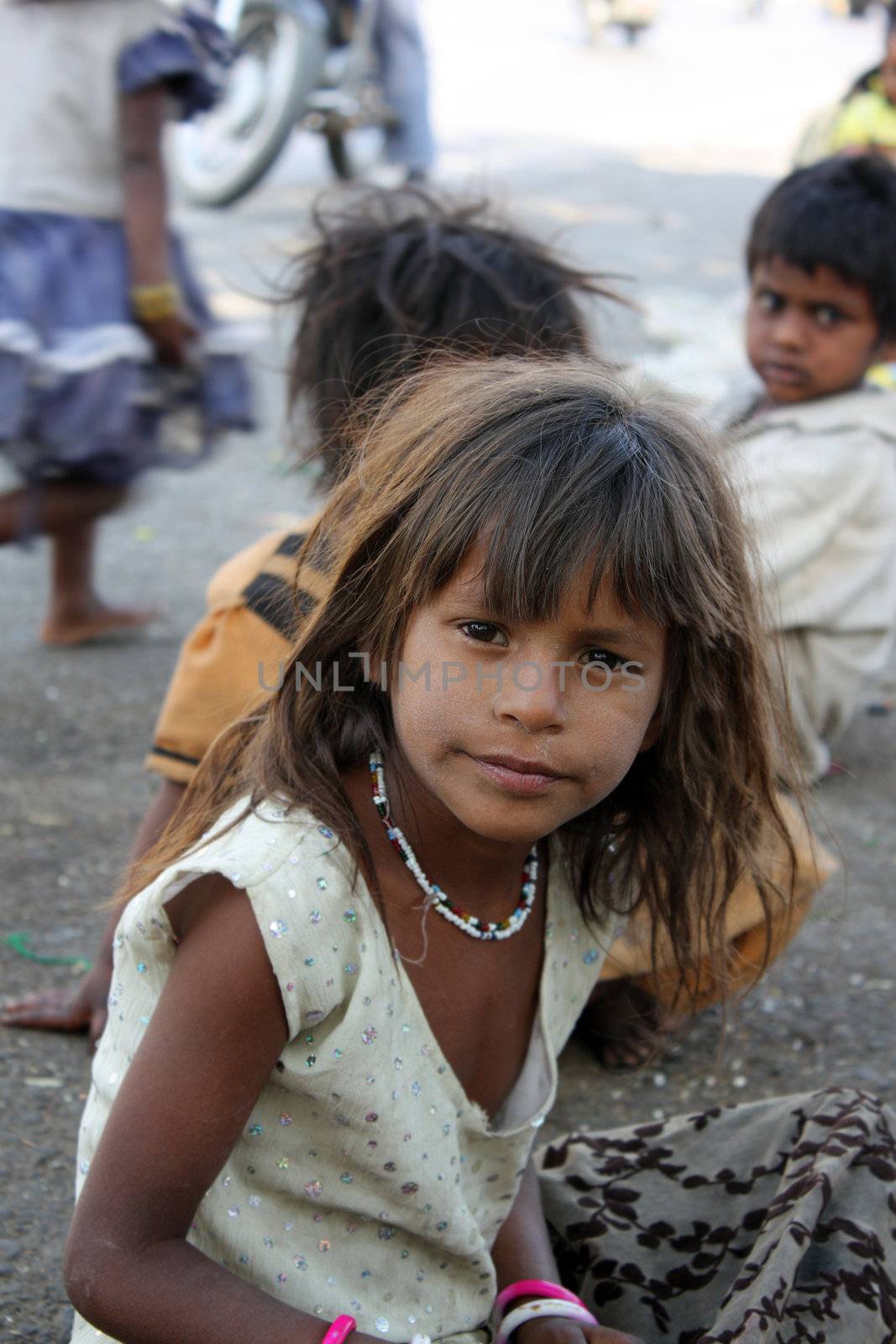 A portrait of an inquisitive beggar girl from India, sitting on the street-side.