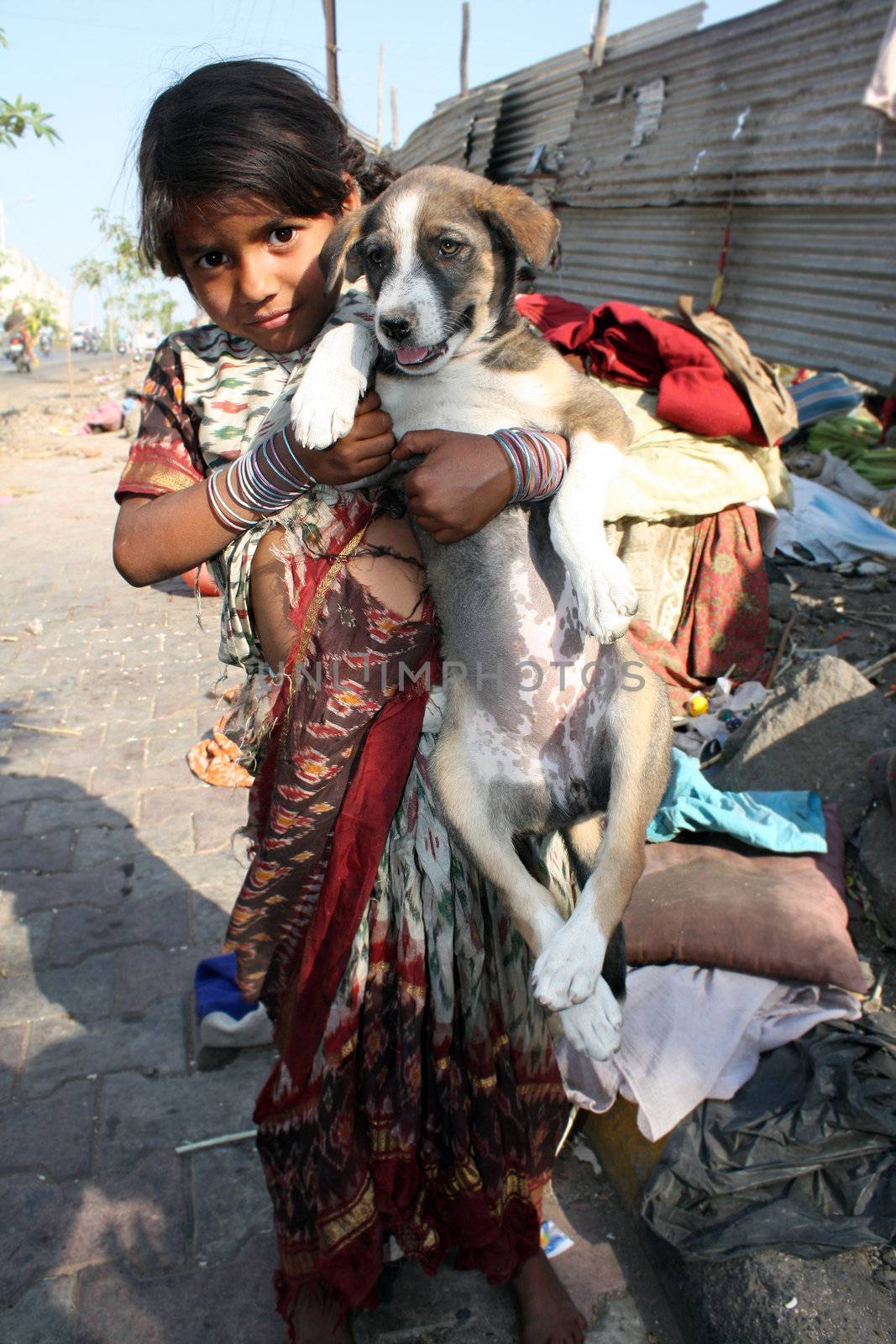 A poor beggar girl from India posing with her street dog, on the street-side.