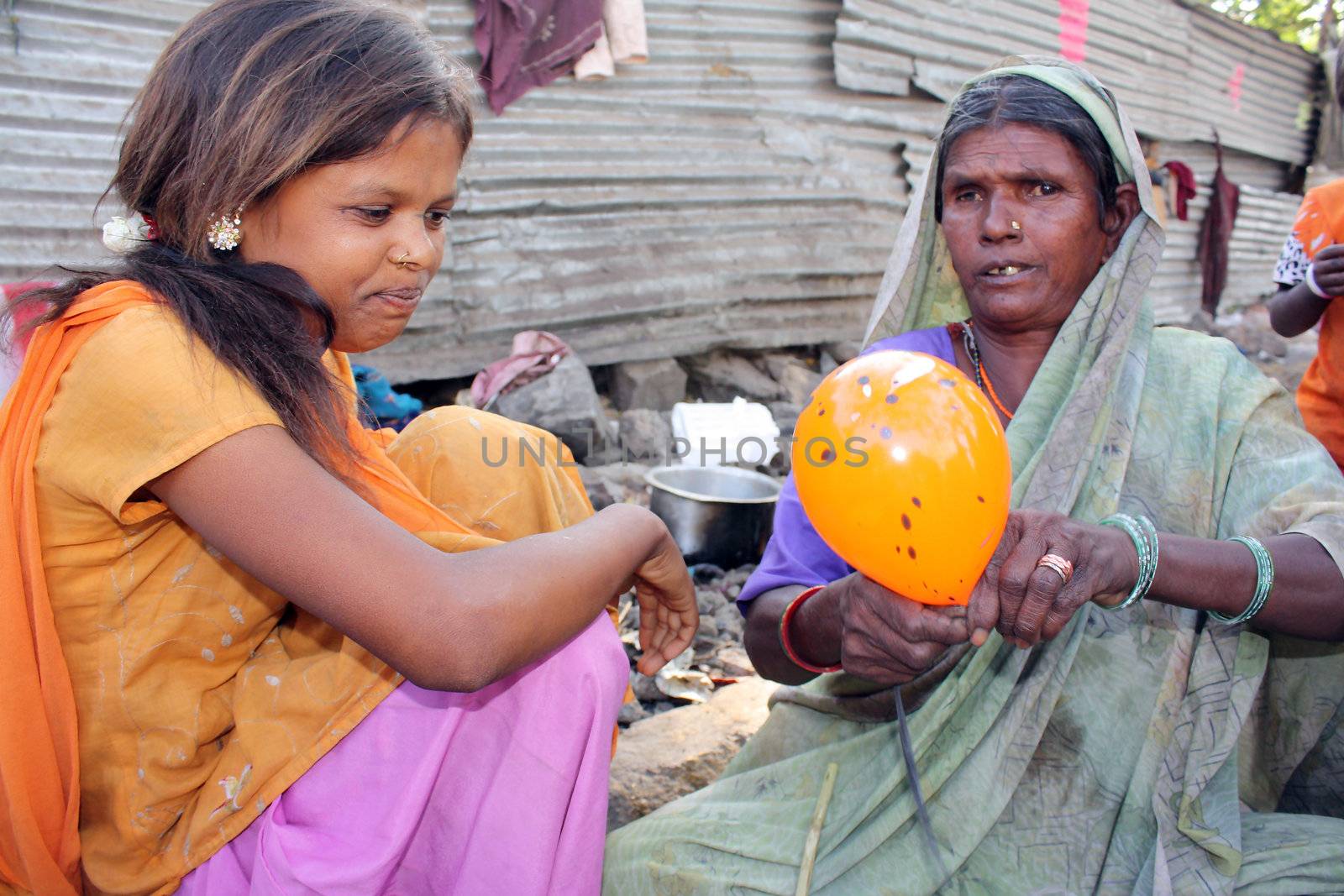 A poor teenage girl who earlier spent her time begging learning how to make balloons and make money from her grandmother. Focus on the teenagers face since the old woman was moving while tying the balloon.