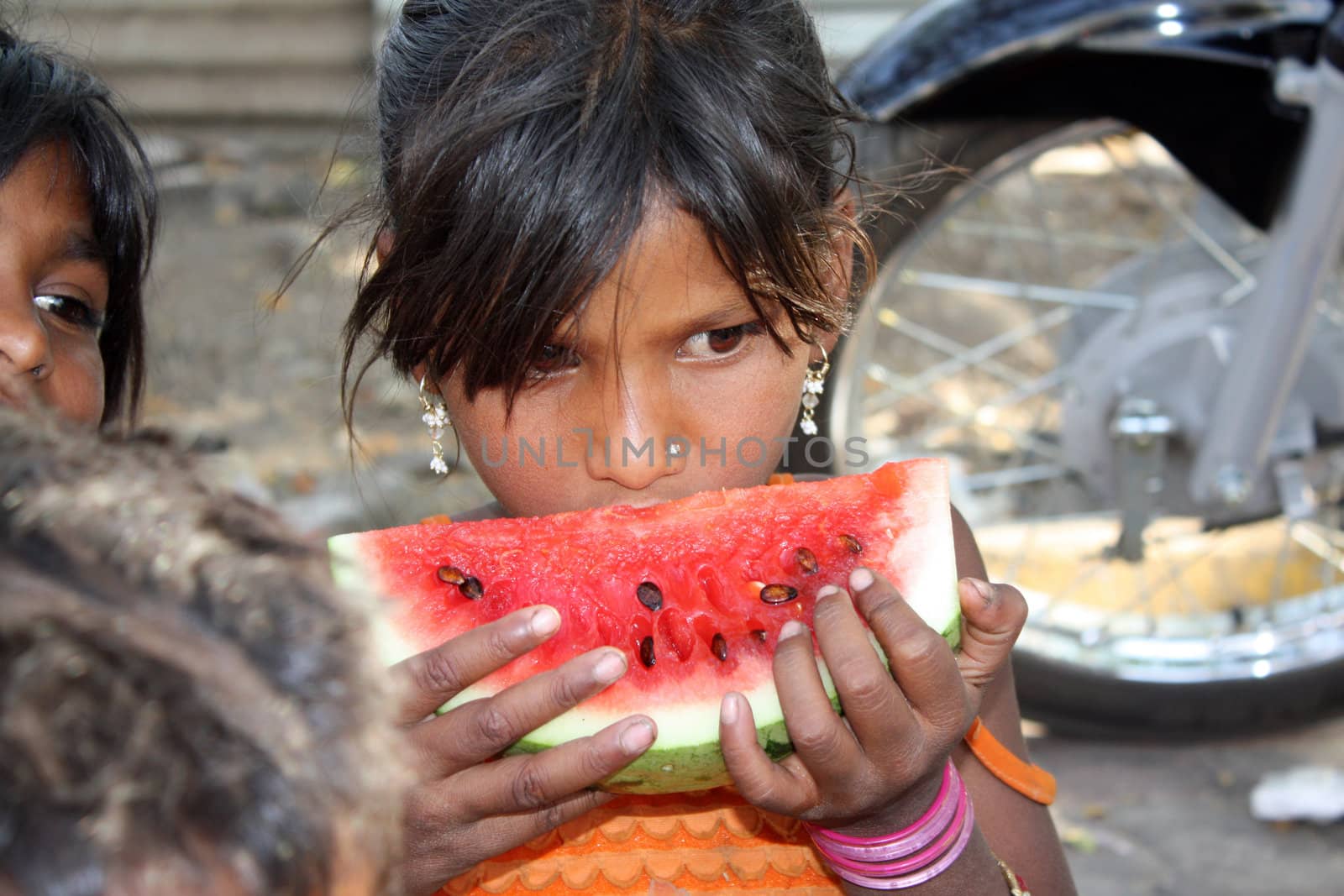 A hungry street-side Indian girl eating a watermelon.