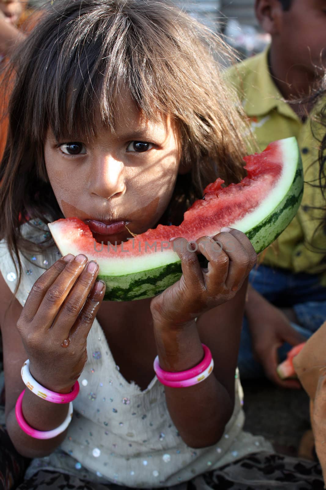 A poor Indian beggar girl hungrily eating a watermelon.