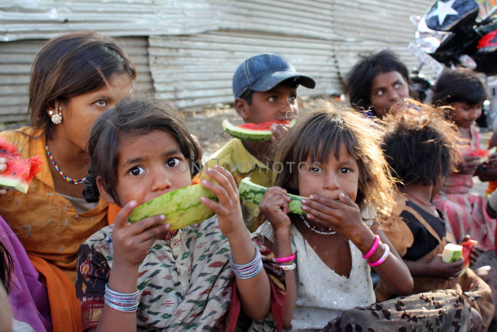 A poor girl in India eating a eatermelon along with her other family who spend their time begging on the streets. Focus on the eyes of the girl in front.