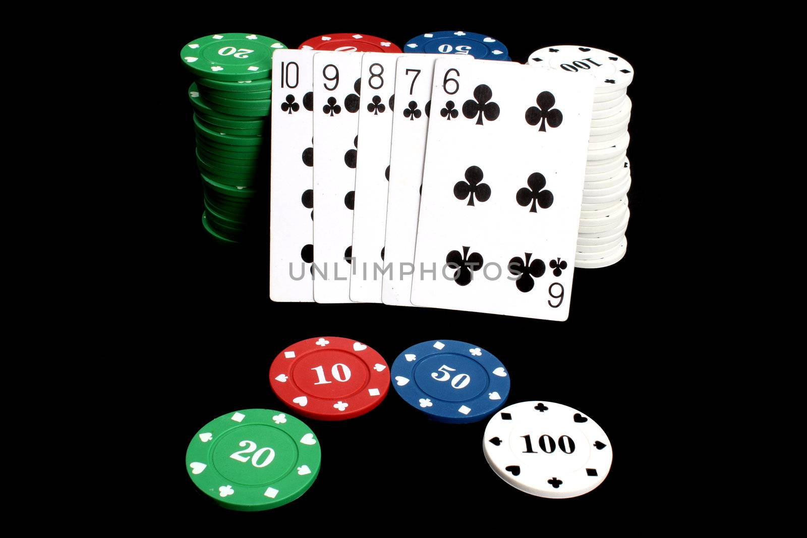 A poker hand of flush consisting of all club cards against gambling chips, on black studio background.