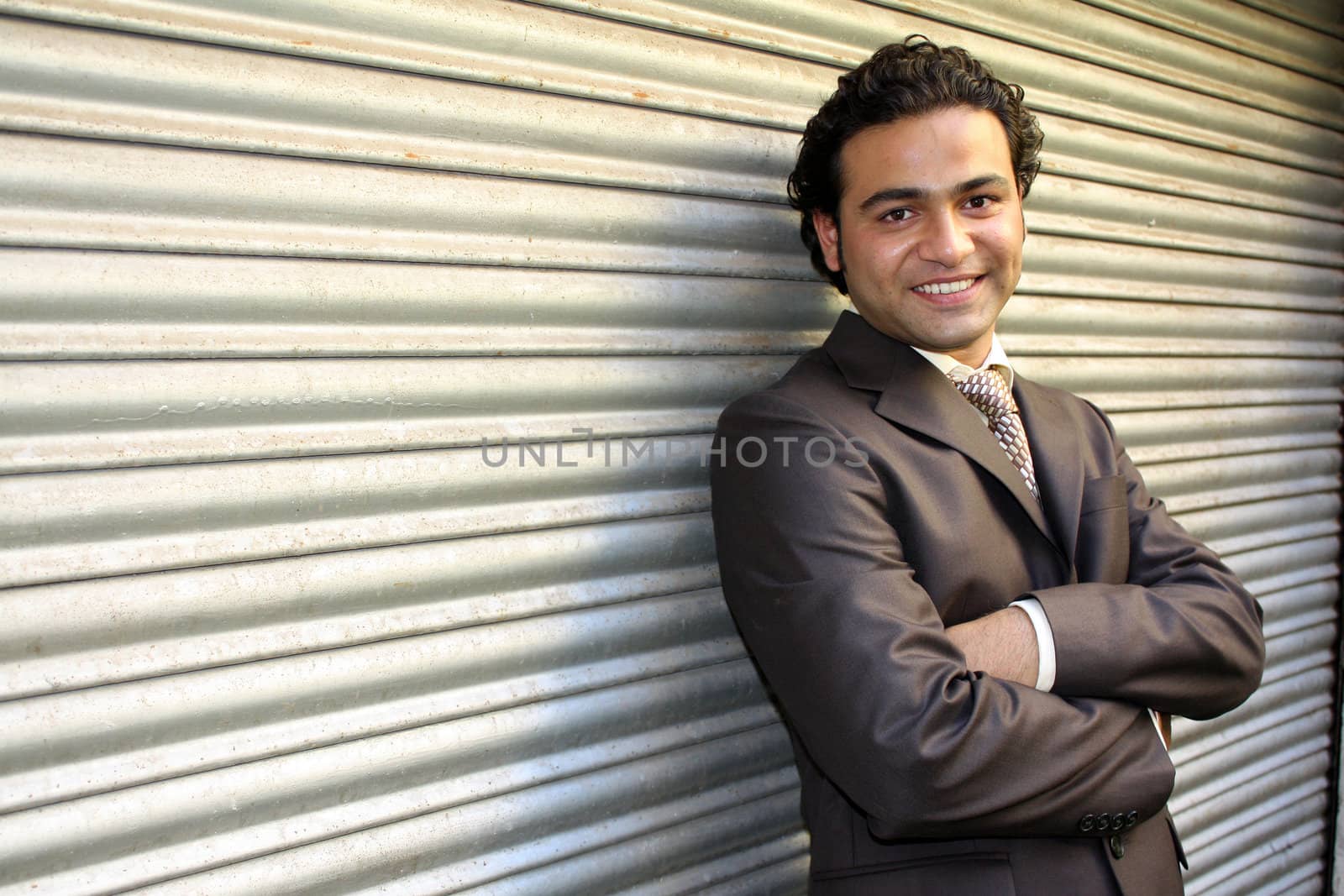 A handsome Indian businessman, posing against a shutter.