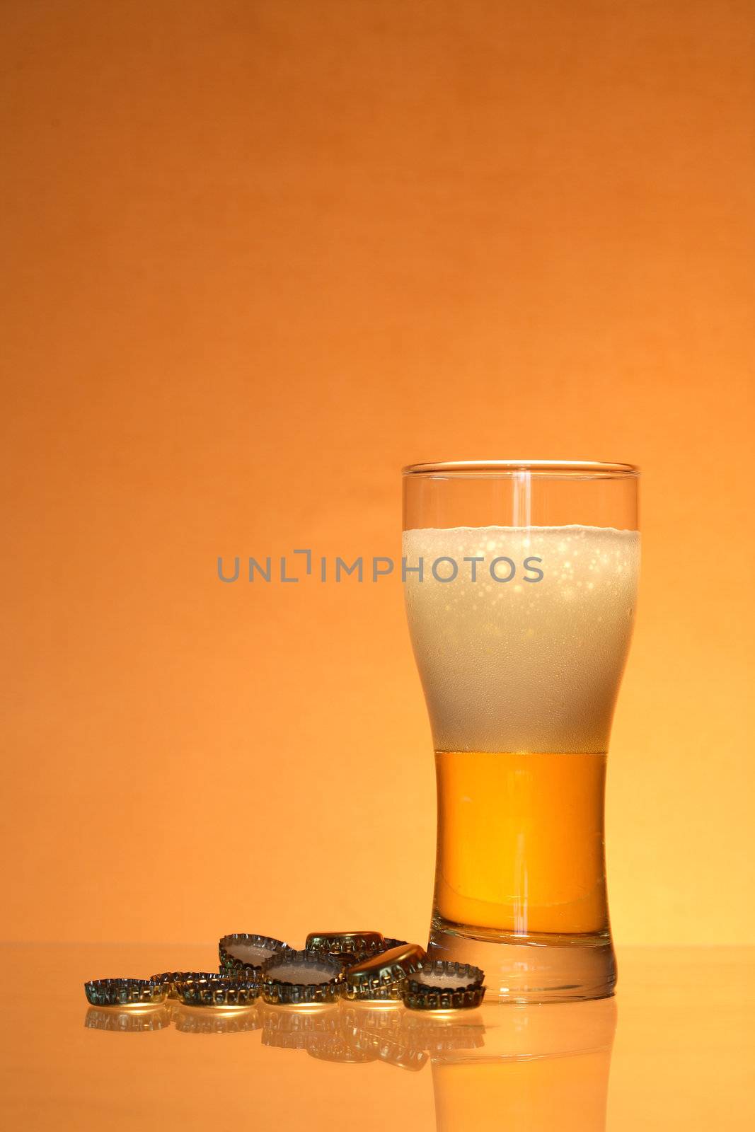 Bottle caps lying near glass of light beer with foam