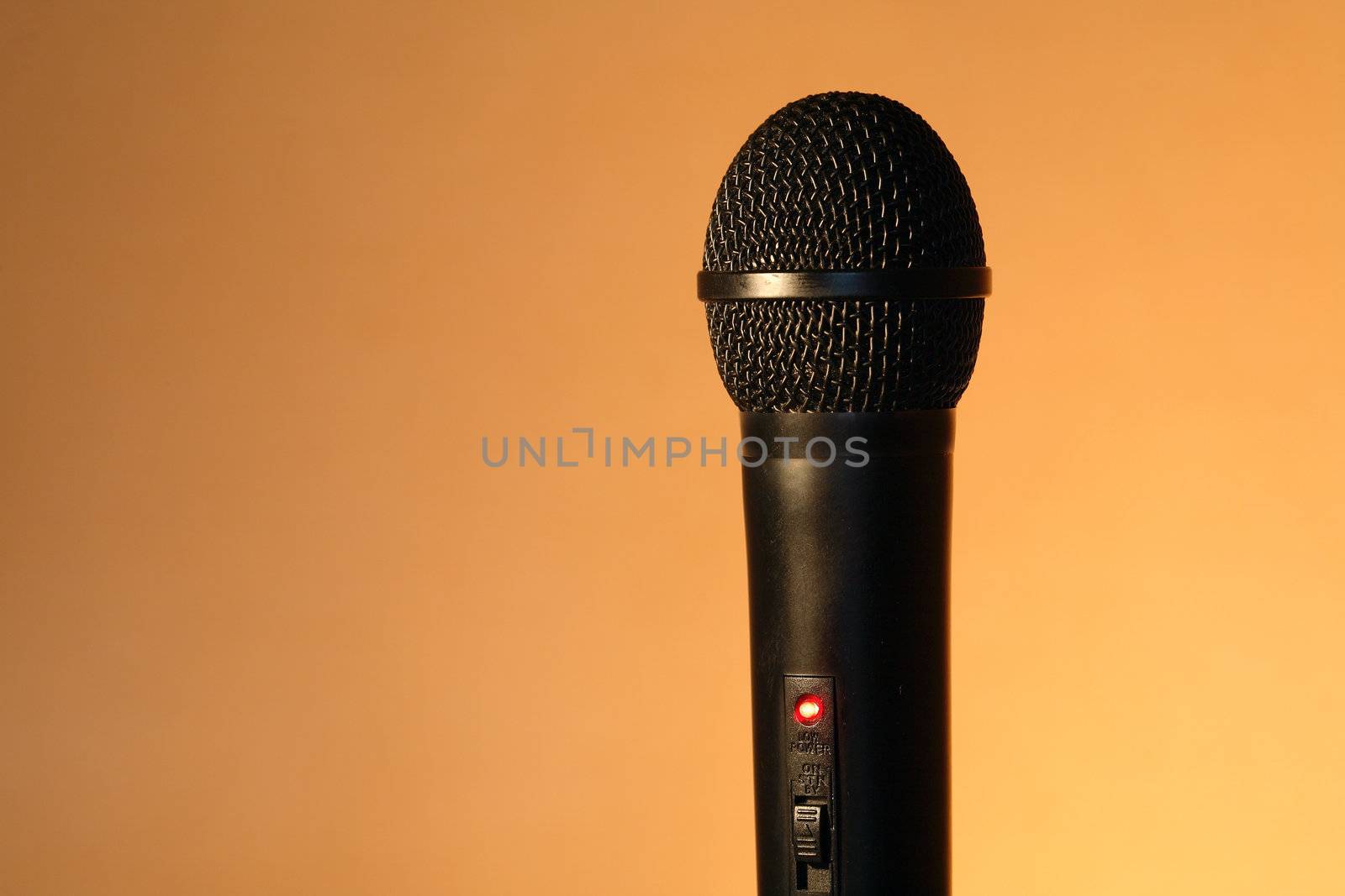 A modern black handheld ball head microphone on ginger background with copy space