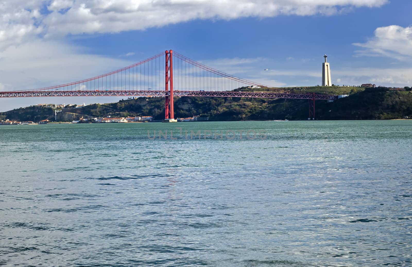 The 25th of April Suspension Bridge in Lisbon, Portugal. Captured from the Tagus River with the Statue of Christ (Cristo Rei)  in the distance.