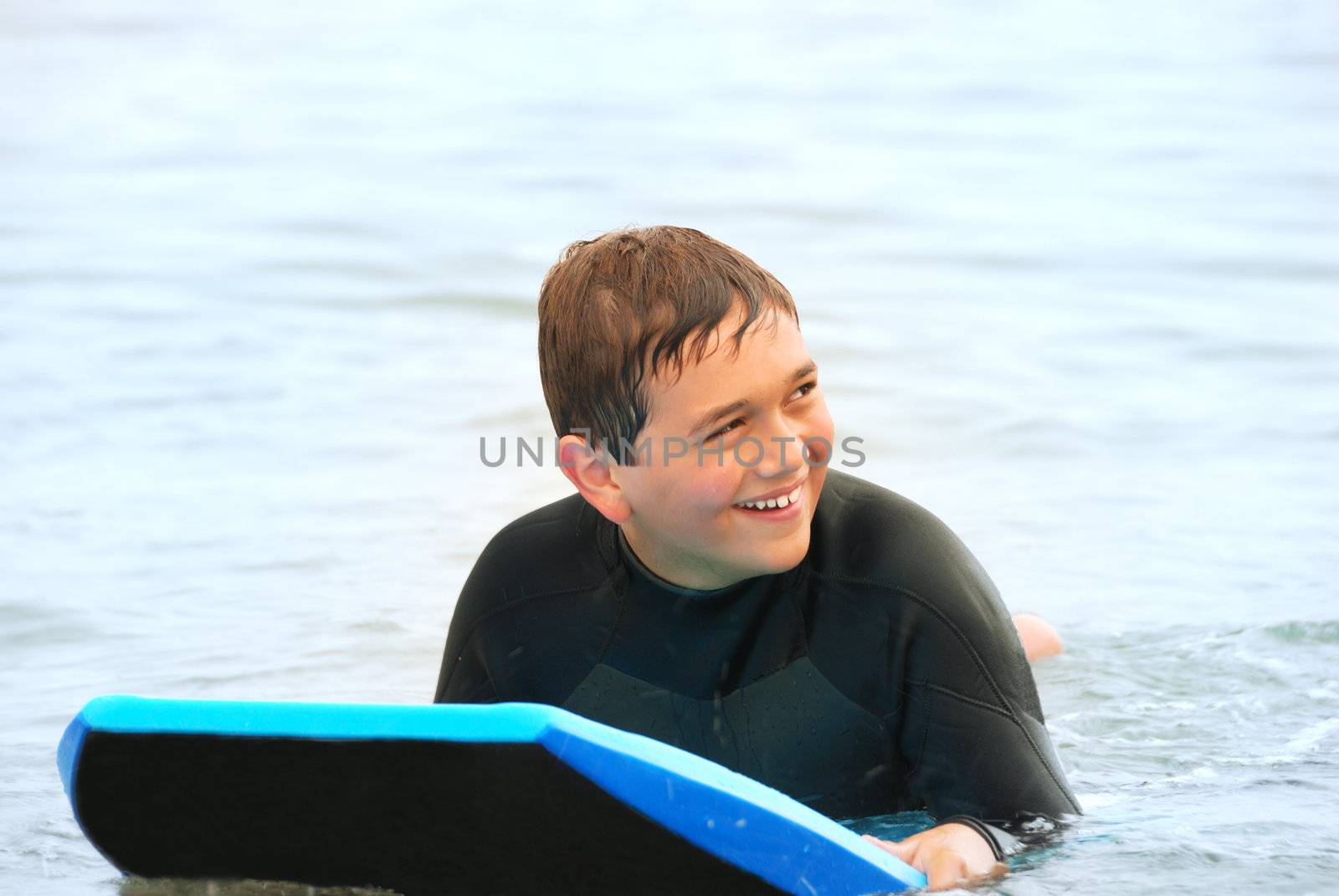 Smiling teenage surfer laying on his bodyboard in the ocean.