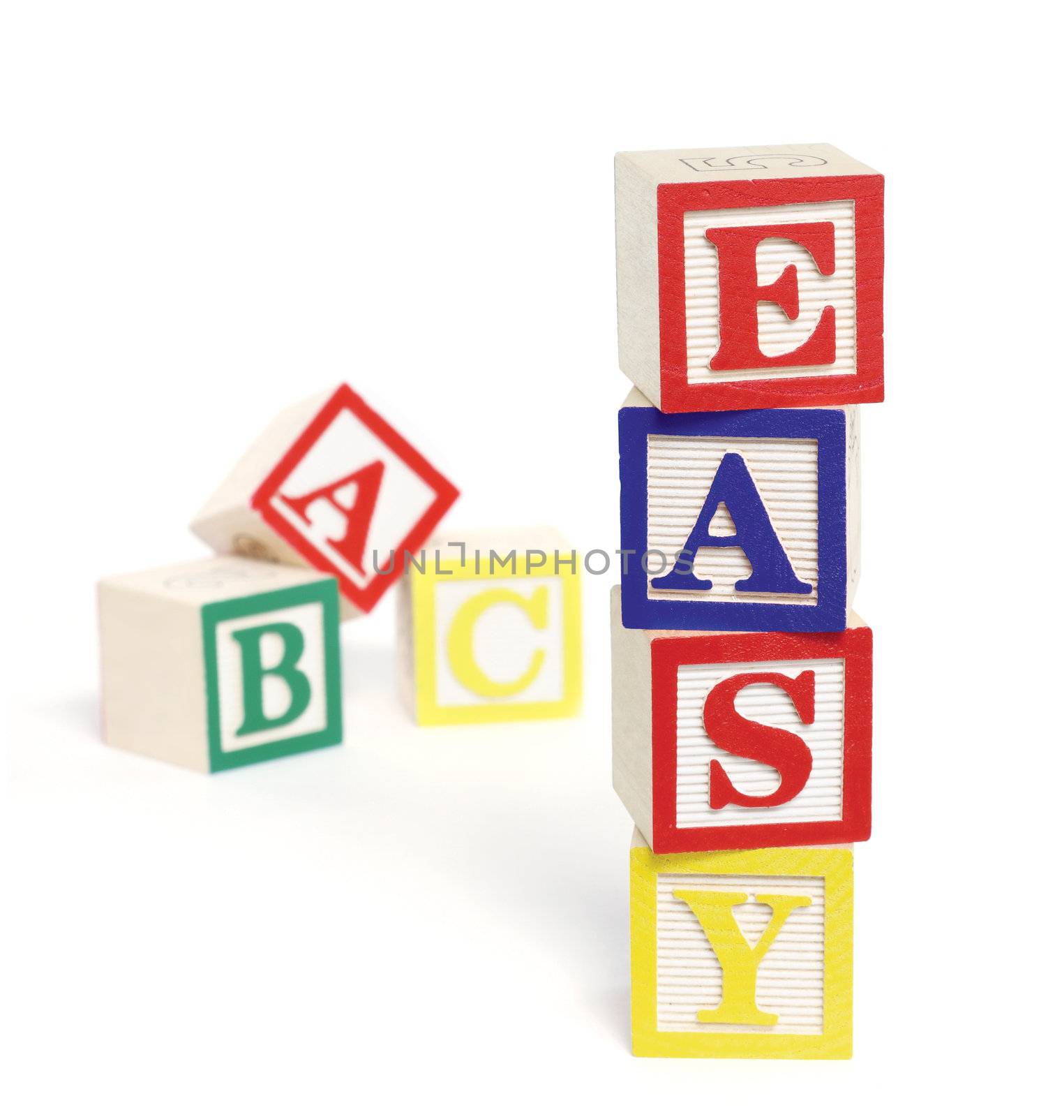 Four wooden alphabet blocks on white background, stacked to form the word, 'easy'. ABC blocks are out of focus in background. Blocks cast shadows. 