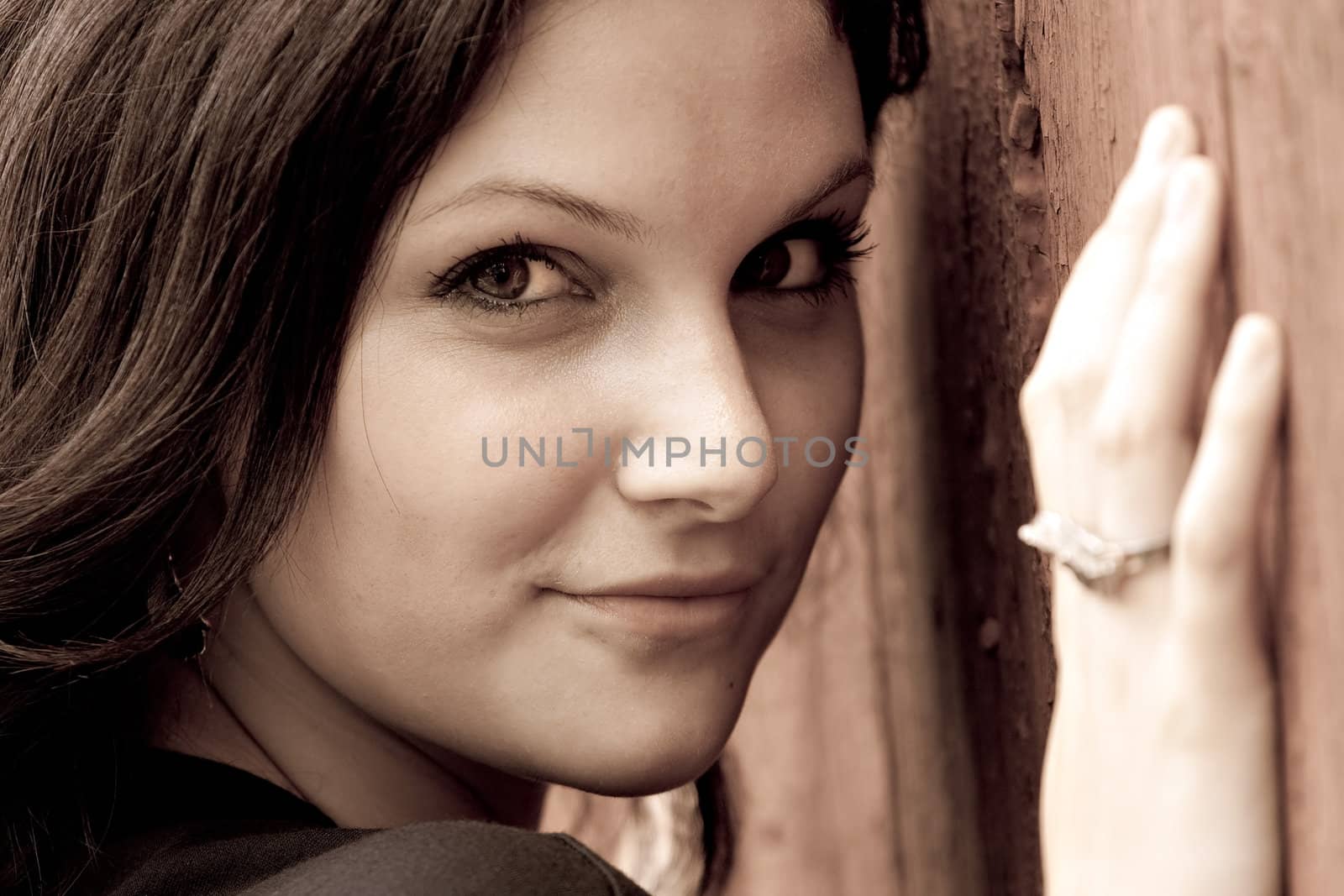 Close up of an attractive young woman in her twenties posing in a rustic country setting in sepia tone. Shallow depth of field.