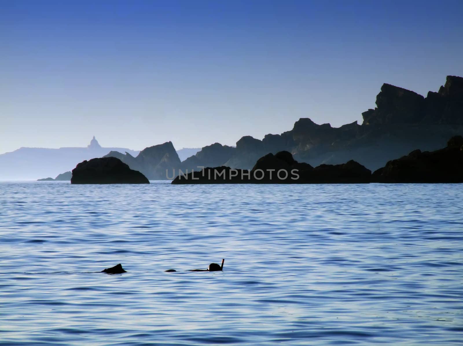 Typical rocky coastline in Malta, punctuated with sheer drops and jagged cliffs, with snorkeller in foreground