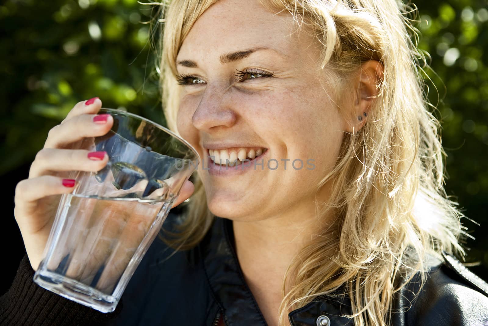 Smiling young woman drinking a glass of fresh water.