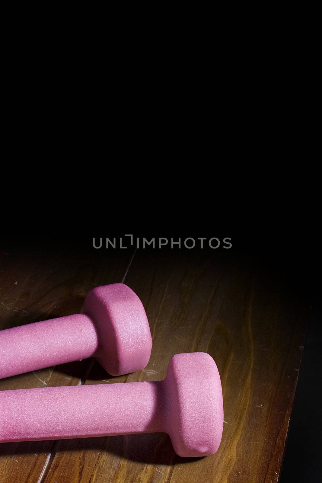 Two pink dumbbells laying on a wooden surface.