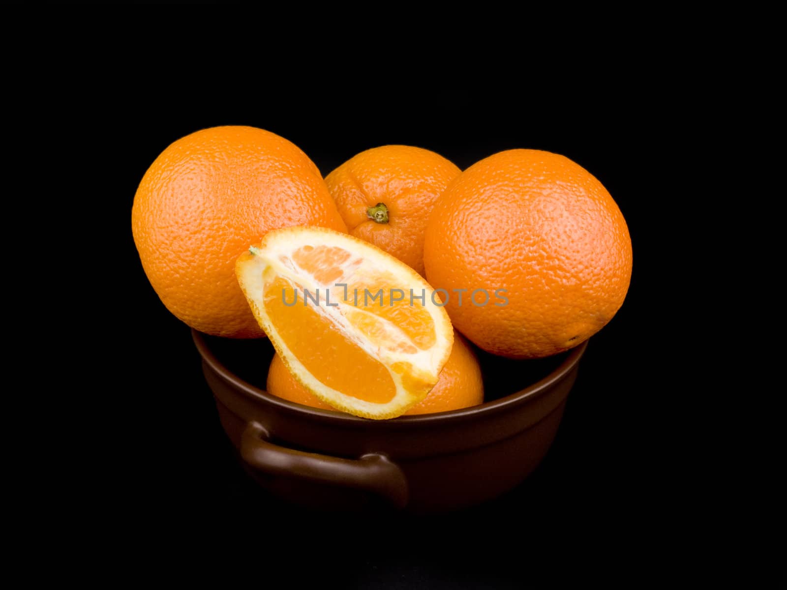Oranges in ceramic bowl on black background