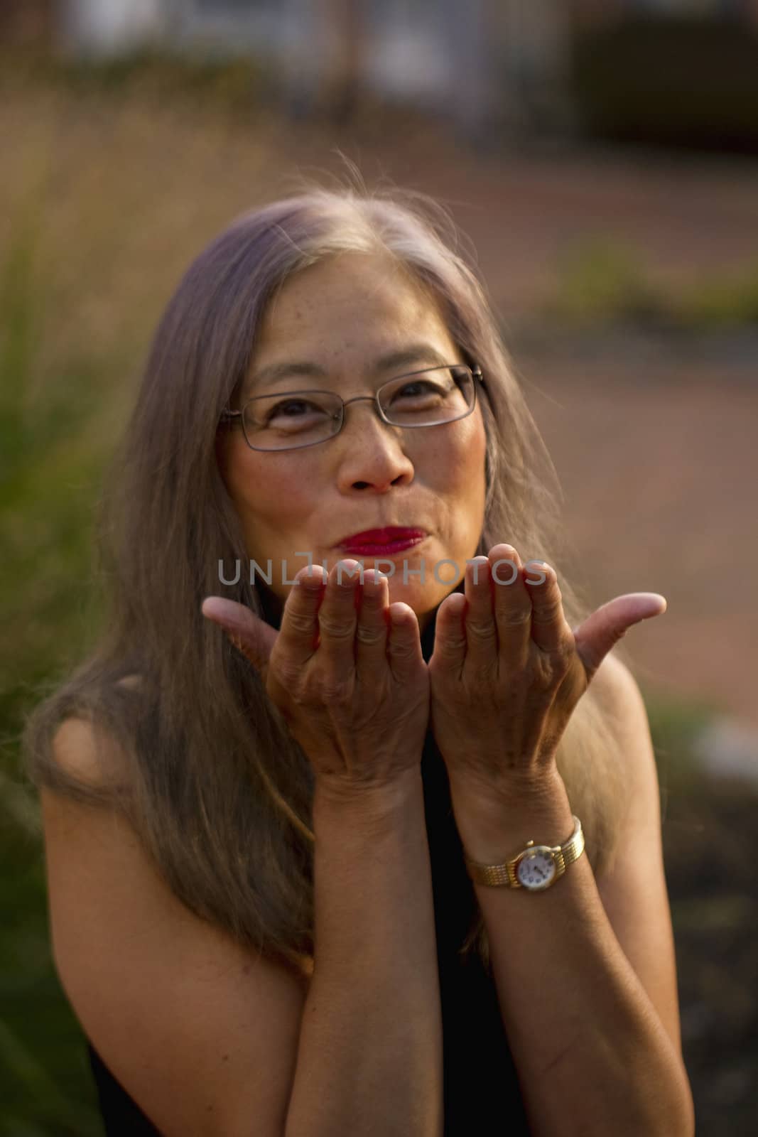 Asian woman with long, gray hair raises her hands to blow kisses