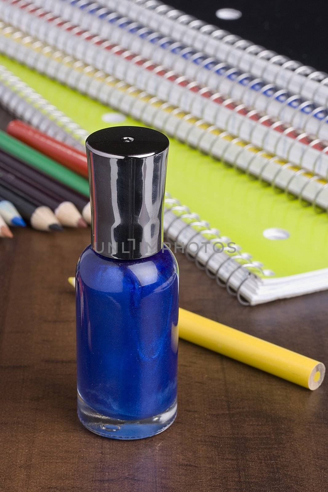 Blue nail polish standing in front of colored pencils and a stack of notebooks.