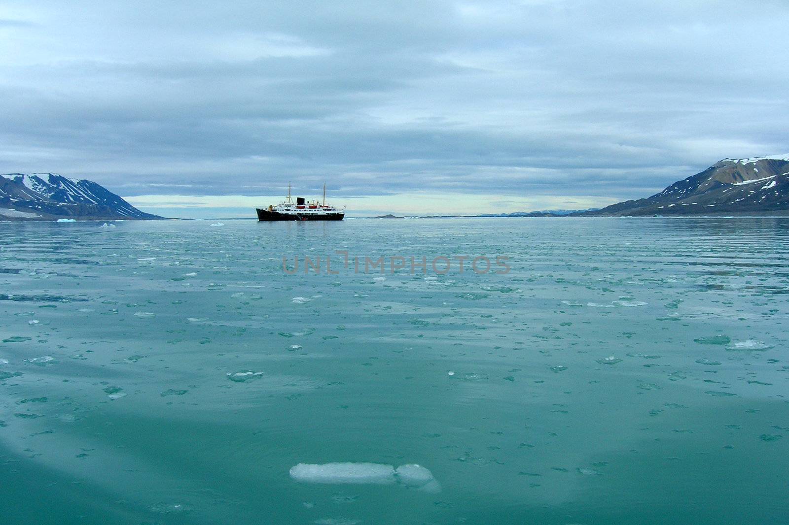 Cruise ship sailing through melting ice and icebergs in a fjord in Spitsbergen, Svalbard.