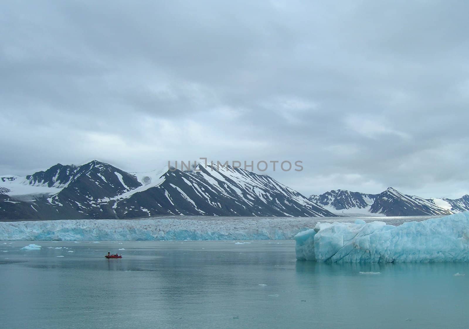 Small rubber boat sailing through melting ice and icebergs in a fjord in Spitsbergen, Svalbard.