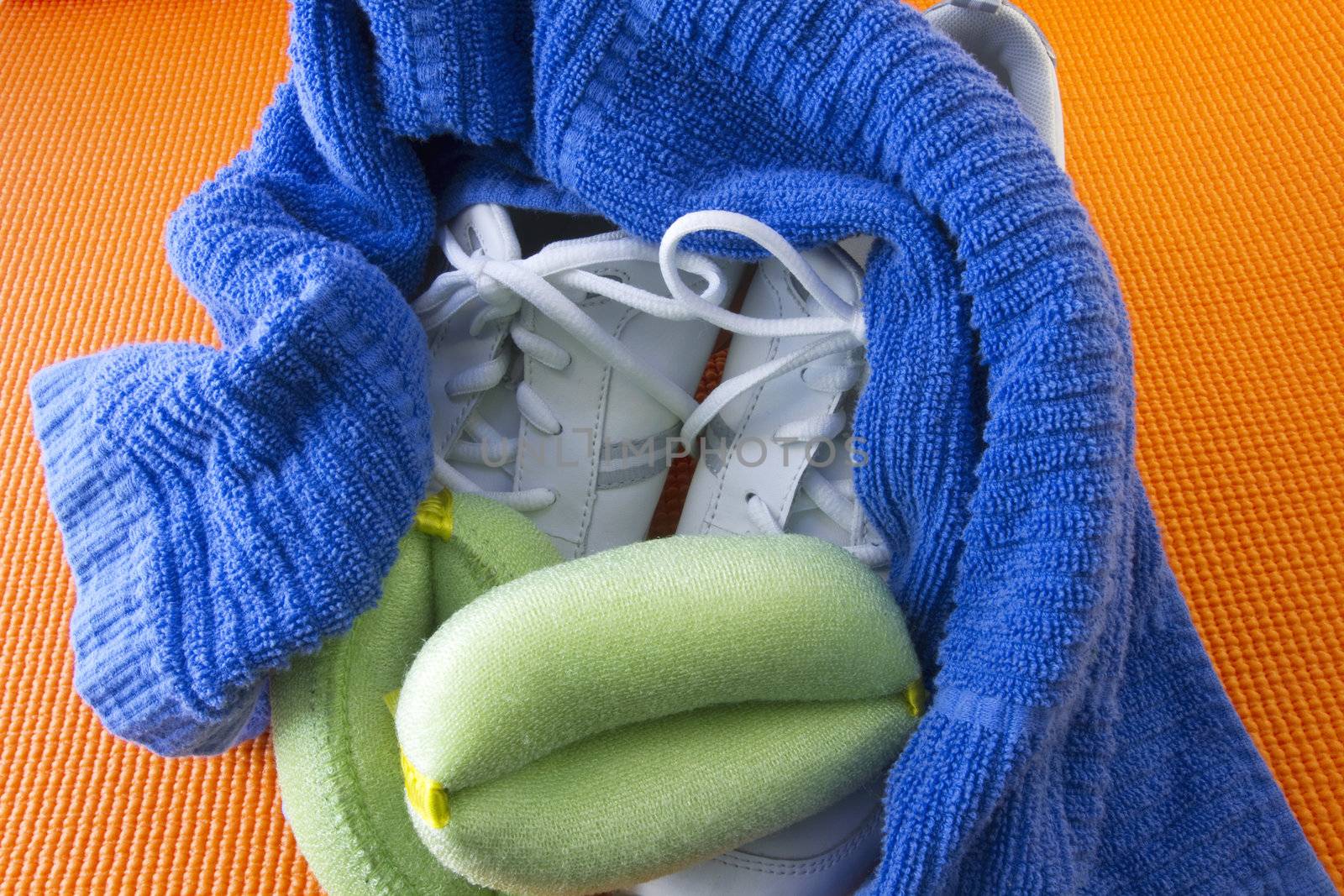 White sneakers, green wrist weights, and a blue towel on an orange yoga mat background reflect exercise readiness
