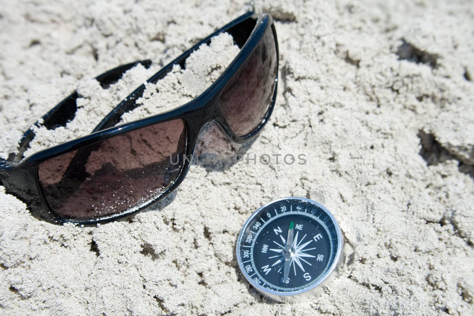 Sunglasses and compass in the sand by Nickondr