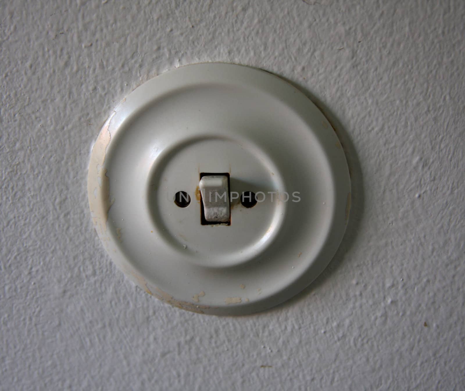 Old round white switch on a white wall.