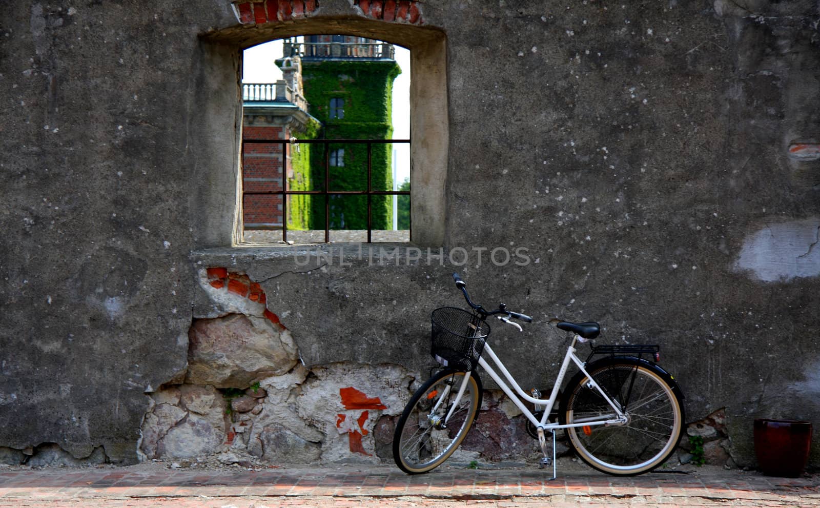 Bike parked by a window in an old wall. A castle is seen in the window.