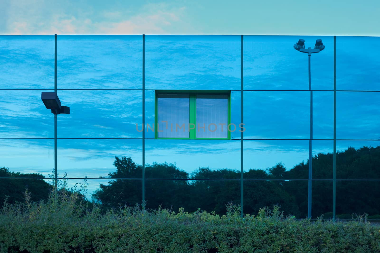 Mirrored image of environment of office building on highly reflective exterior wall with window.