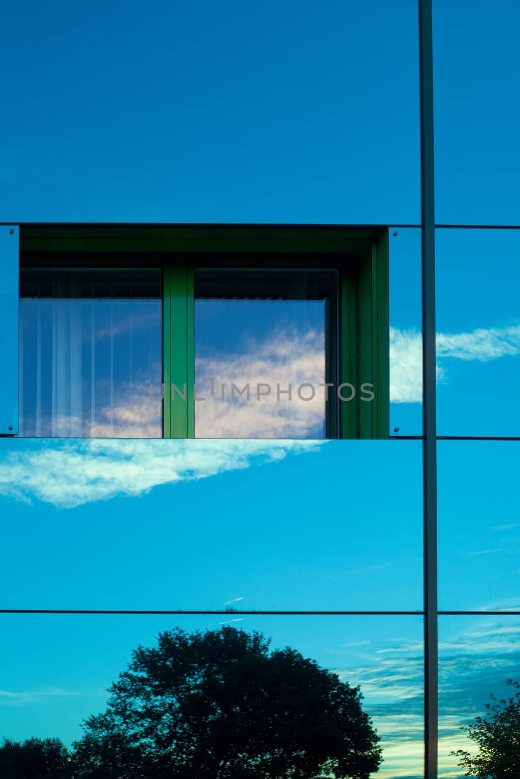 Mirrored image of environment of office building on highly reflective exterior wall with window.
