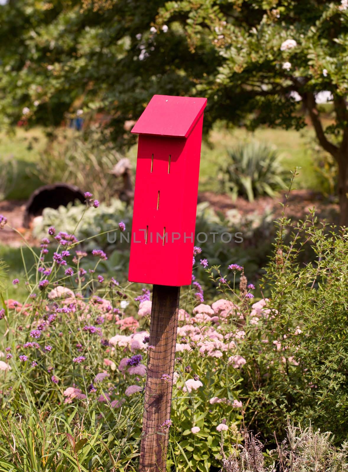 Red painted bird house in flowery garden with small slits for the bird to enter