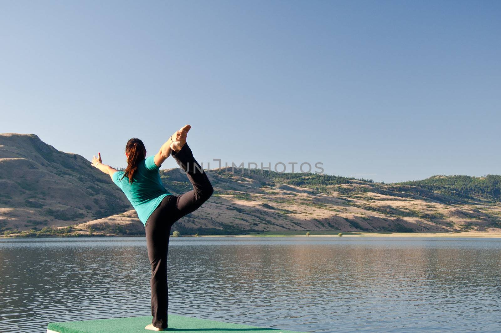 Young fit girl practicing Yoga in the Dancers pose next to a calm lake