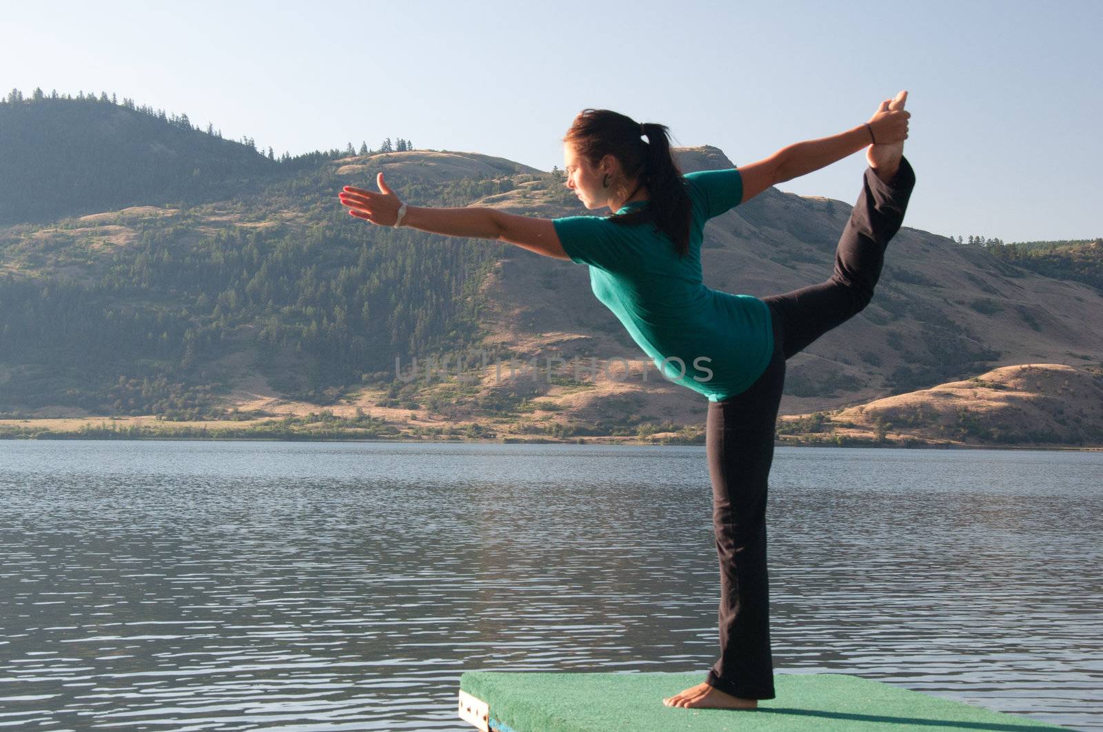 Young fit girl practicing Yoga in the Dancers pose next to a calm lake