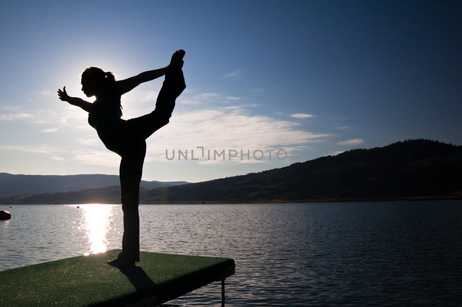 Silhouette of a beautiful young girl doing a dancers pose by a lake
