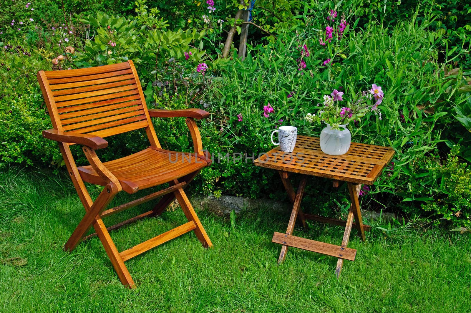A hardwood garden chair and table, cup of coffe and a vase with flowers.
