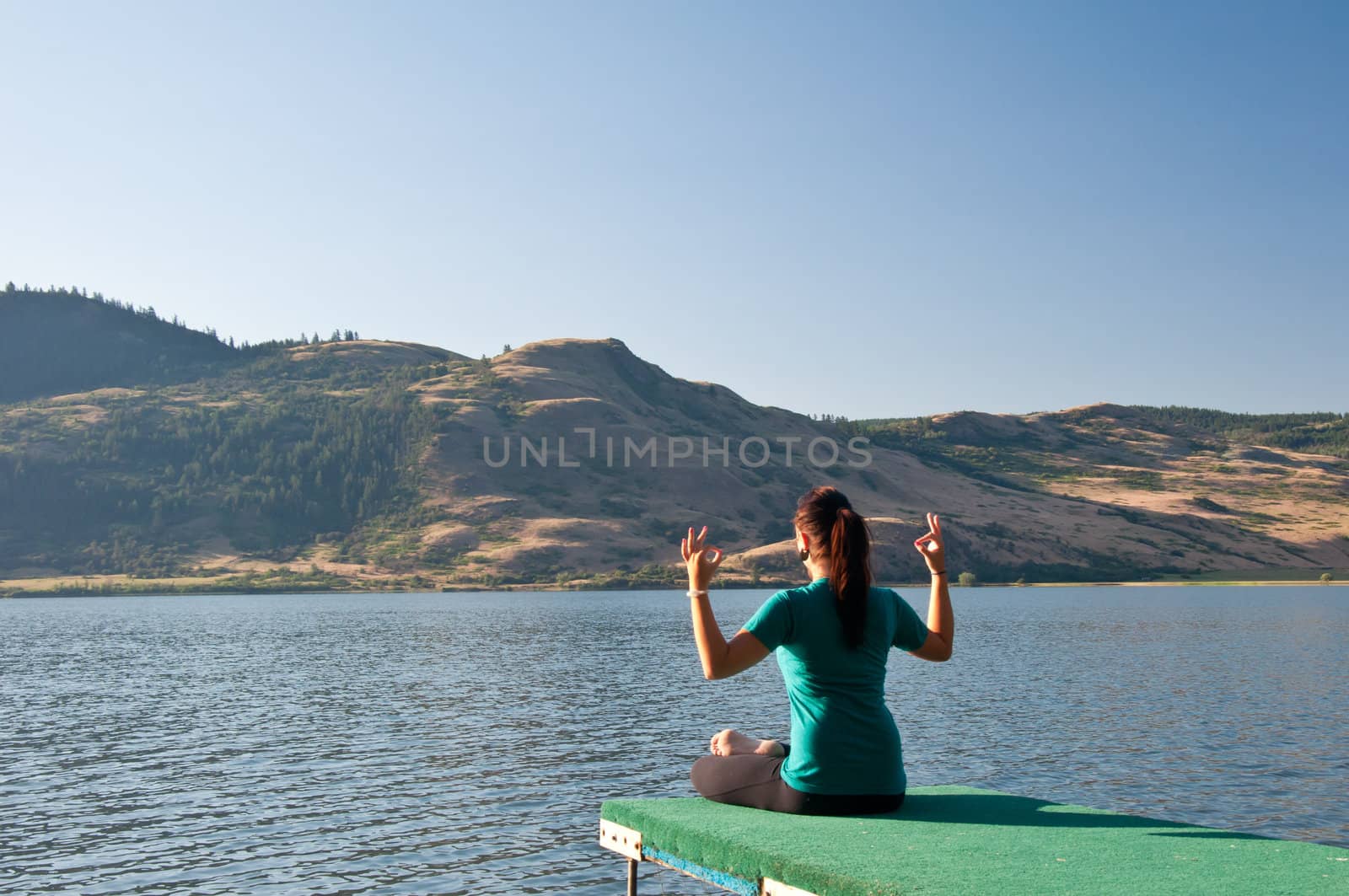 Young fit girl practicing Yoga by meditating next to a calm lake