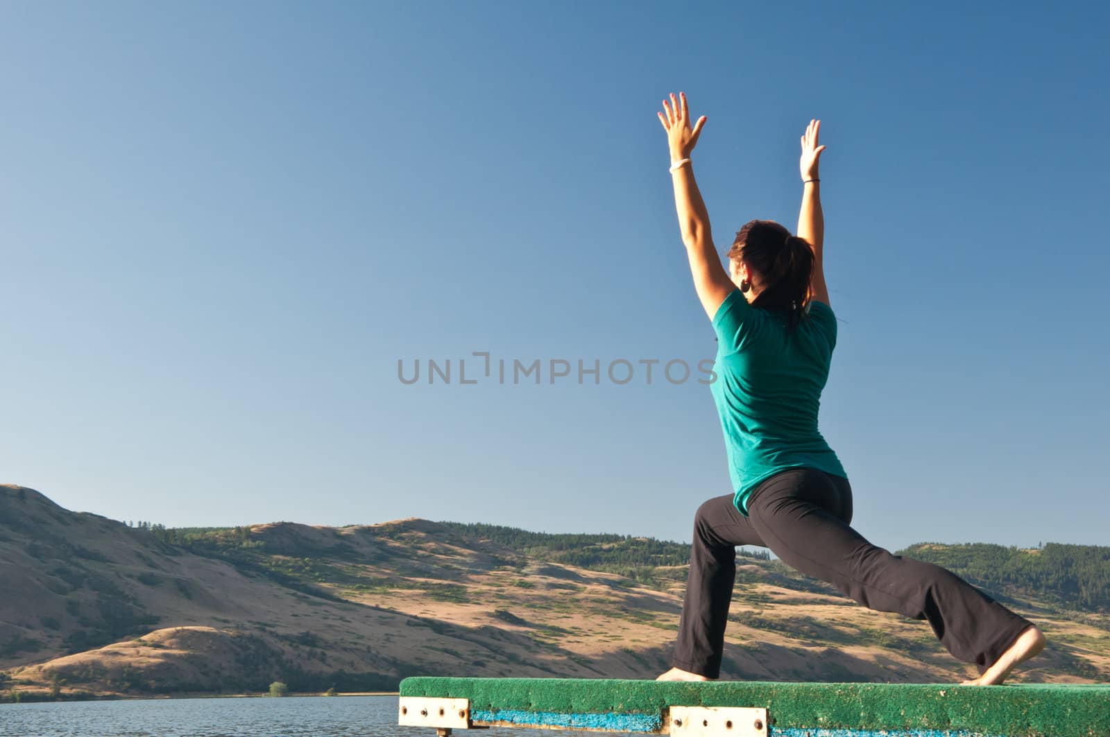 Young fit beautiful girl practicing yoga outside in the Warriors pose next to a calm lake