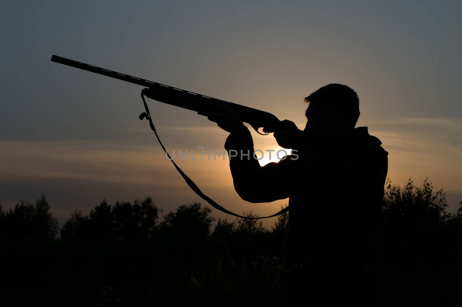 Silhouette of the hunter with a gun against the evening sky.