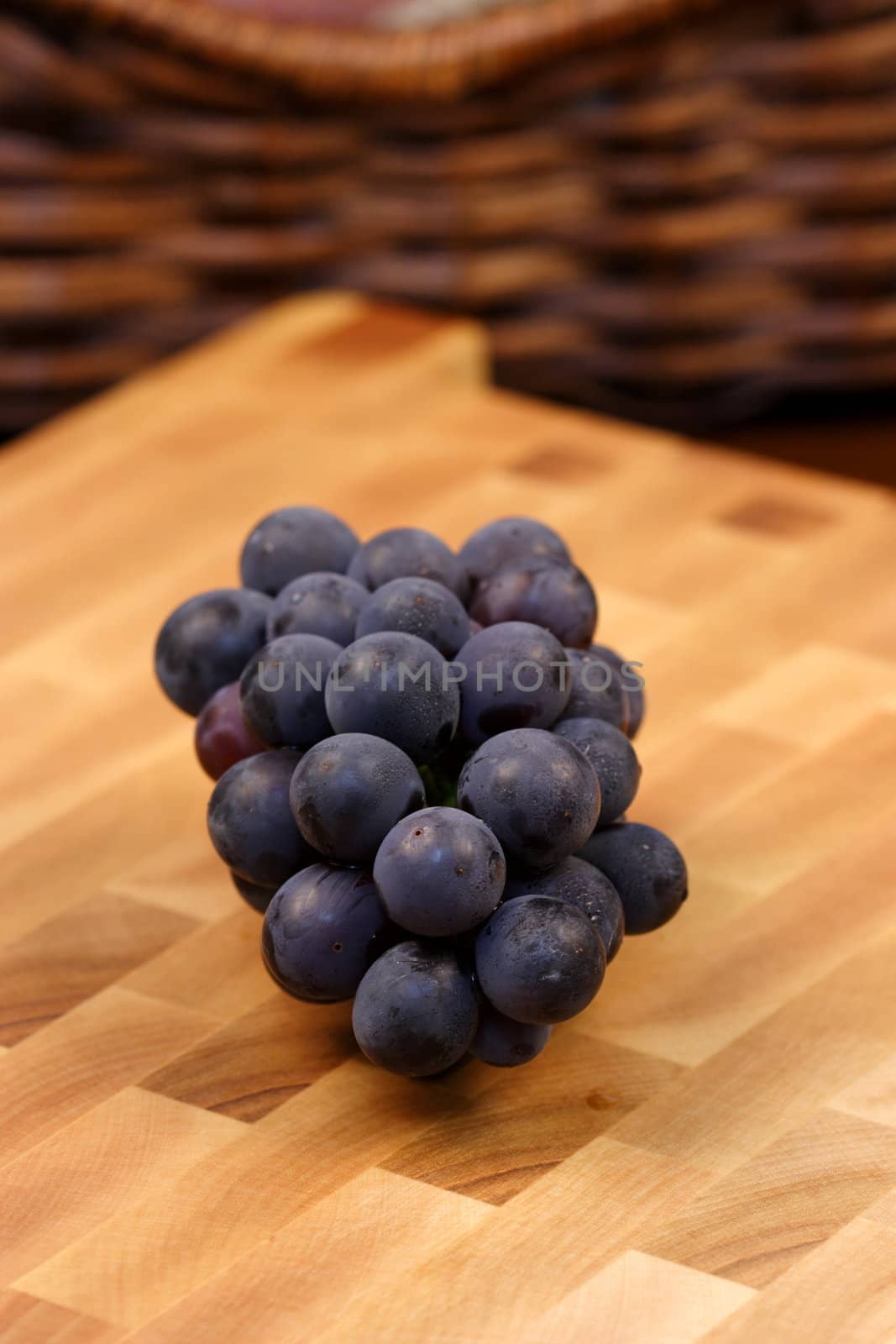grapes on fine wood cutting board with red wine and bread basket on background 