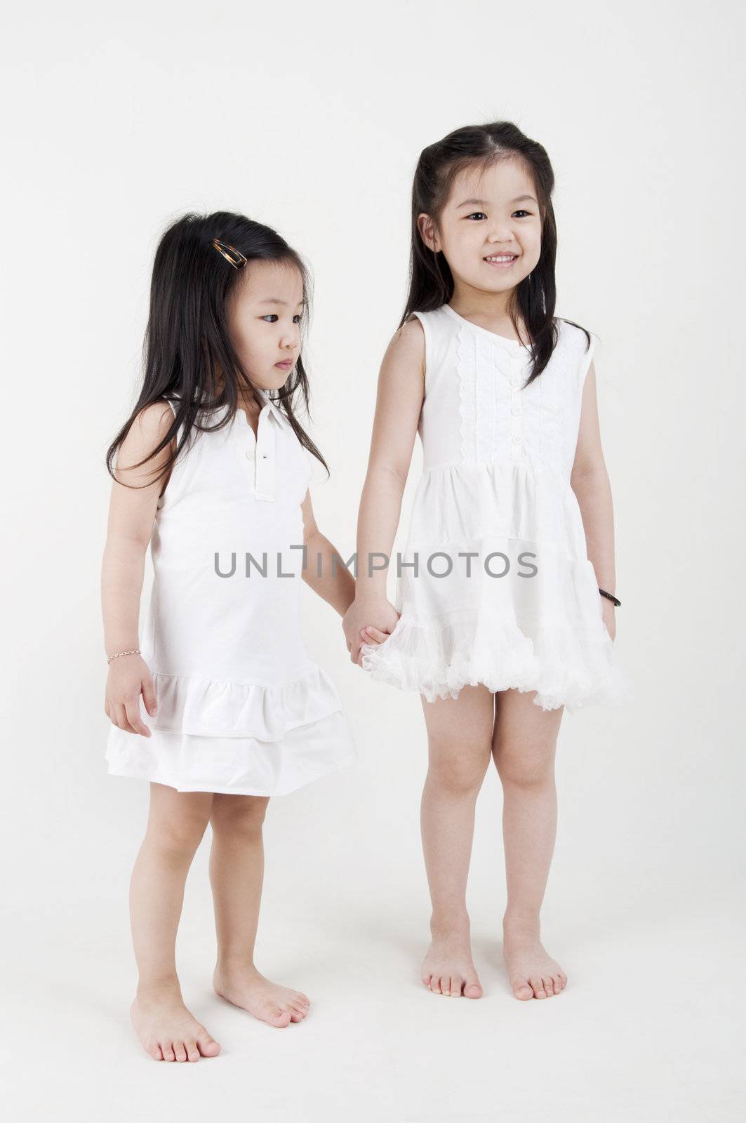 Asian sisters holding hand on plain background