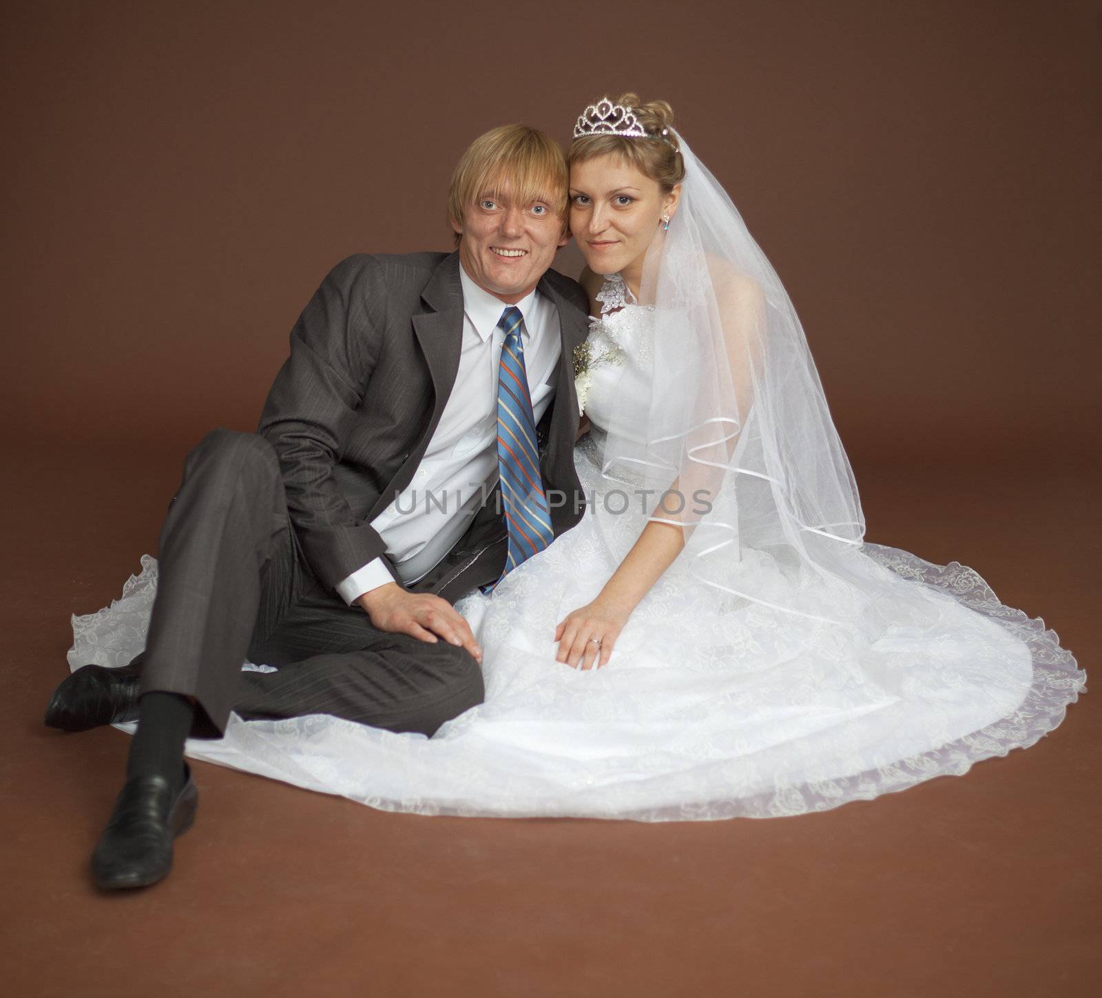 Happy newly-married couple sits on a brown background