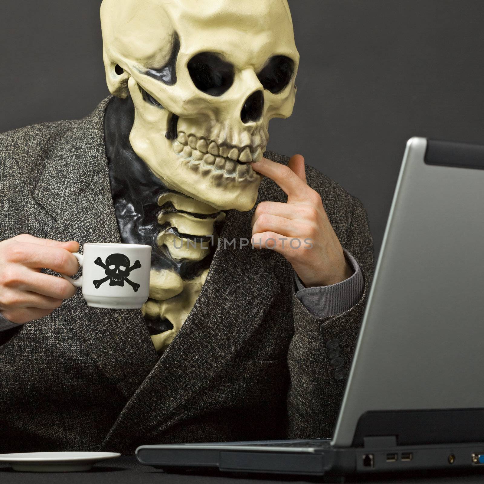 The skeleton drinks poisonous coffee sitting at a table with the laptop