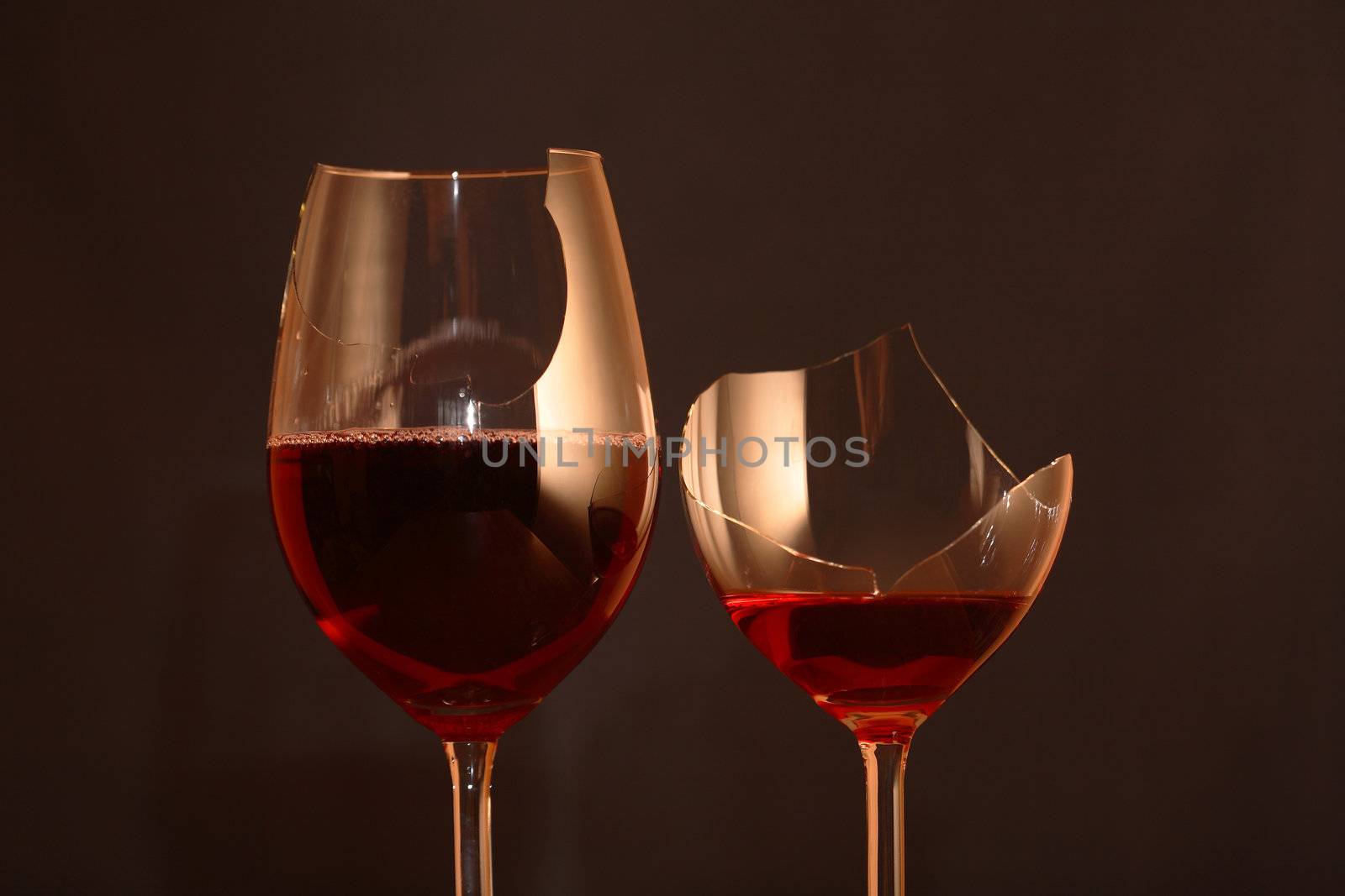 Two broken goblets with red wine on dark background