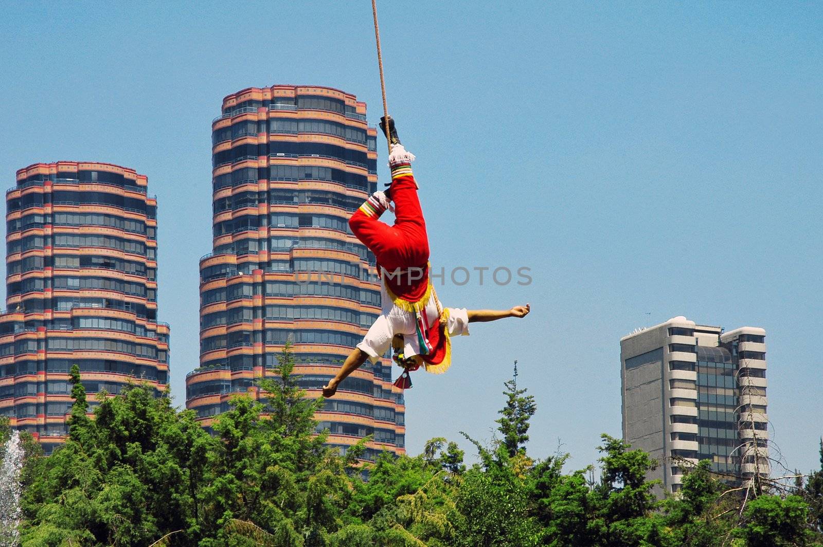 Builder hanging by one leg up side down on the rope with Mexico city on background