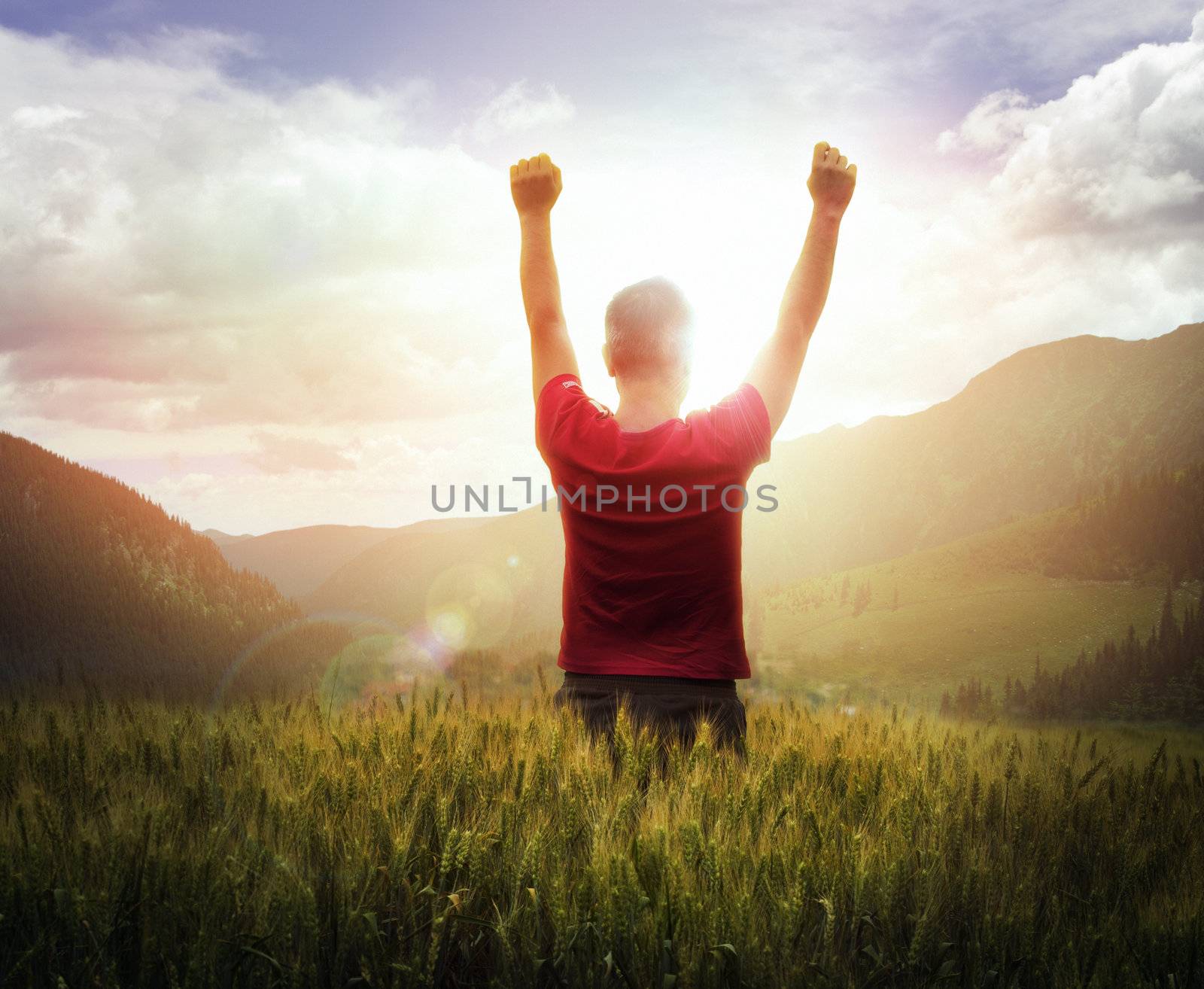 Young man with arms raised looking at sunset with mountains ahead