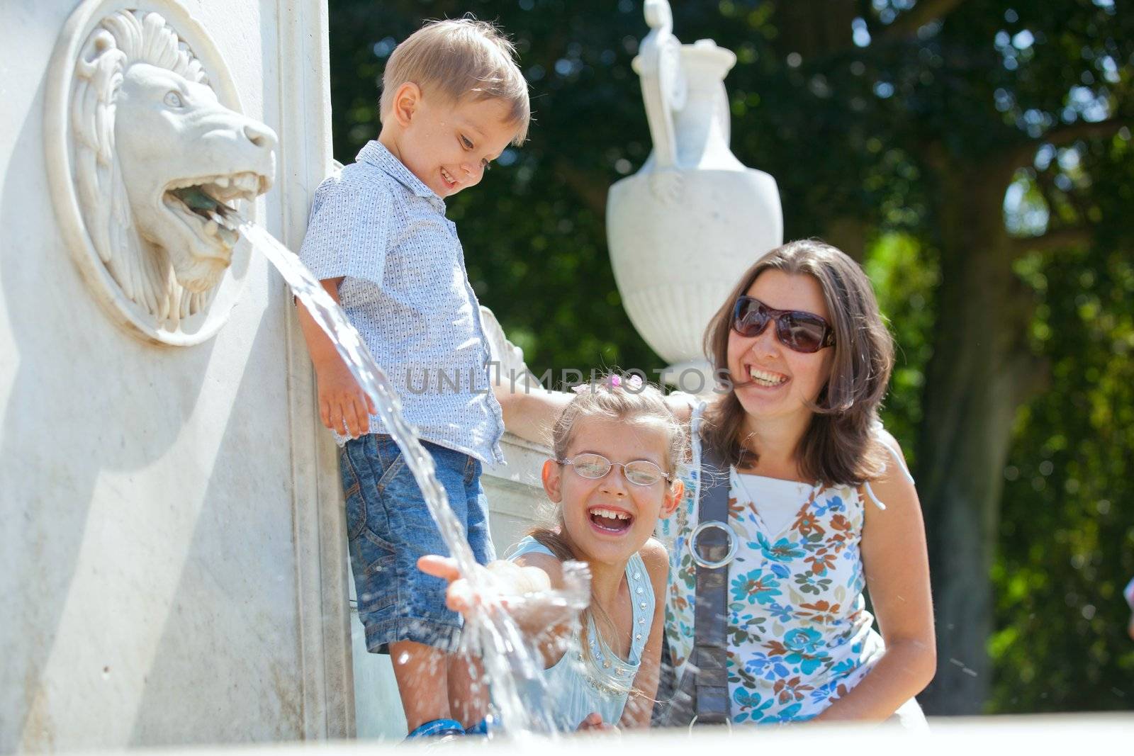 Beautiful Mother with her kids playing with water in fountain
