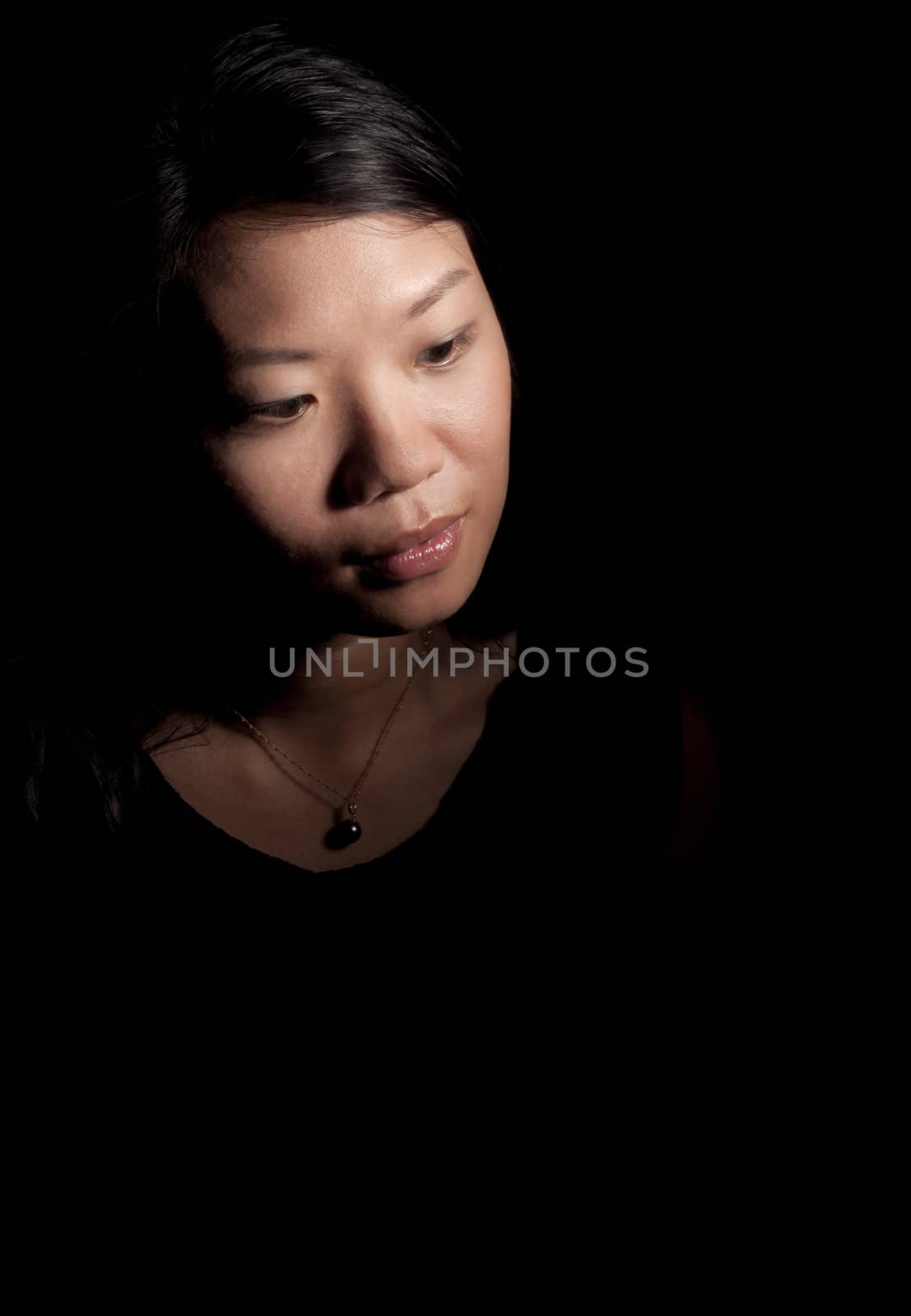 Soft contemplative look of beautiful asian woman on black background