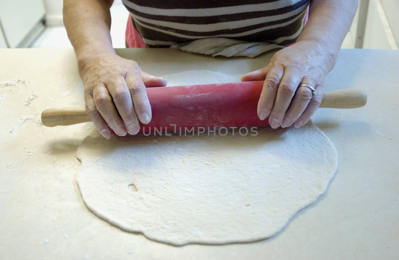 elderly woman using rolling pin on pizza dough   
