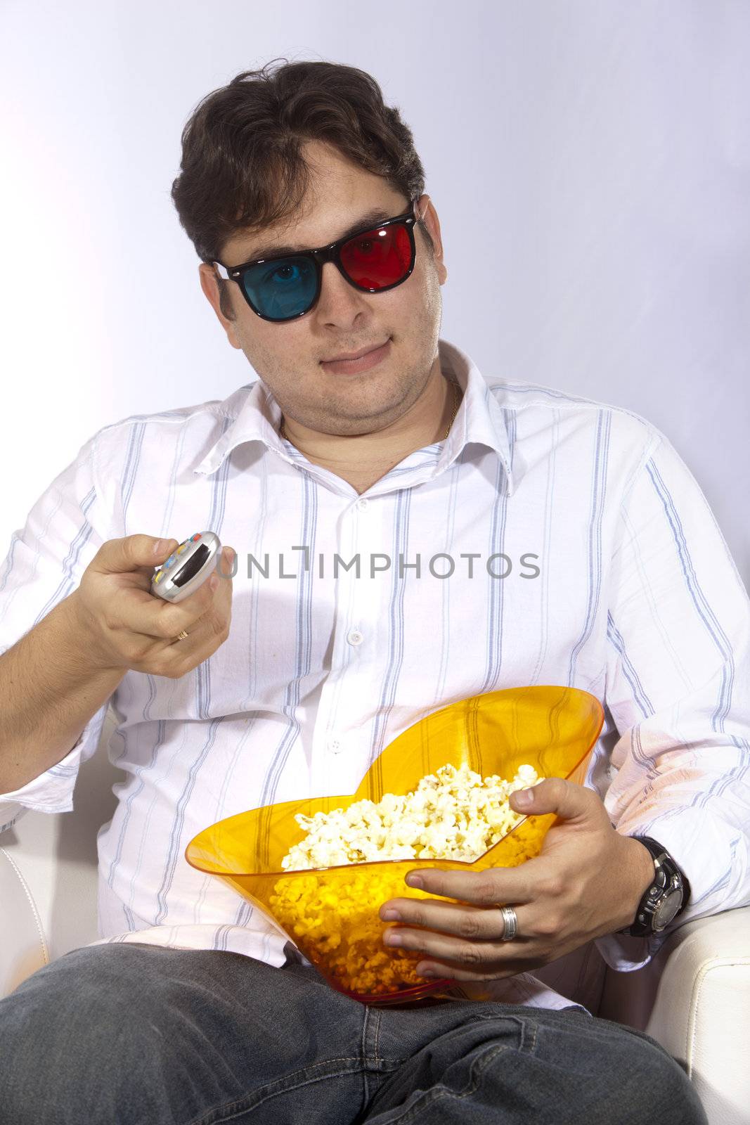 A young man watching a movie in 3D, with stylish 3D glasses and eating popcorn.